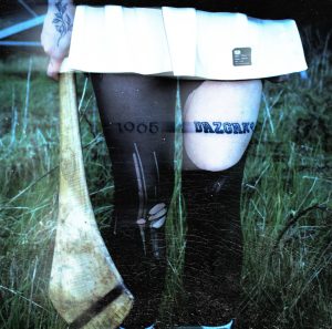 azGak! - Stimpy EP artwork: a lo-fi film photograph of a person's legs in dark tights, one thigh bearing a DazGak! tattoo in varsity lettering, holding a hurley stick, shot on grass